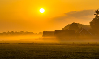 Amanecer sobre un parque vacacional con alojamientos glamping, campos tranquilos y neblina matinal.