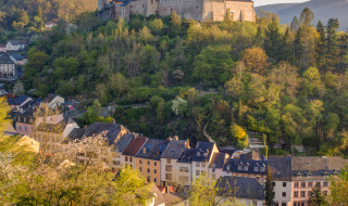 A hilltop castle overlooking a quaint village, surrounded by green hills and trees in golden sunlight.