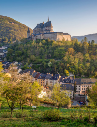 Un castello arroccato sovrasta un caratteristico villaggio, immerso tra colline e alberi verdeggianti.