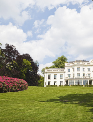 Wit landhuis omringd door groene gazons en bloeiende struiken op een vakantiepark met glamping.