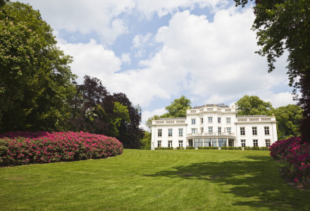 Wit landhuis omringd door groene gazons en bloeiende struiken op een vakantiepark met glamping.