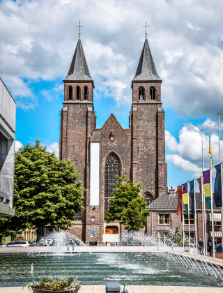 Et foto af en historisk kirke med tvillingetårne og springvand foran, taget nær Lathum, Gelderland, Holland.