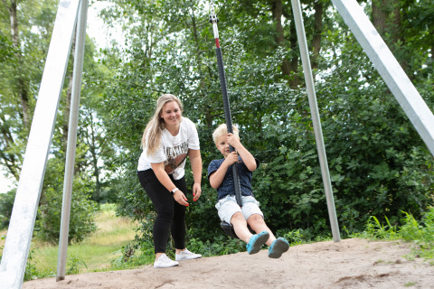 Vrouw speelt met kind op een kabelbaan in Holiday Park 't Rheezerwold, omgeven door bomen in Overijssel.