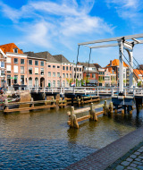 Brücke über einen Kanal mit historischen Gebäuden und Booten im Hintergrund in einem Ferienpark.