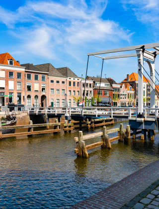 Puente levadizo sobre canal con casas históricas y barcos en un parque vacacional holandés soleado.