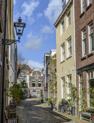 Encantadora calle adoquinada entre casas históricas, bicicletas y plantas bajo un cielo azul soleado.