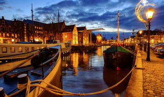 Vista nocturna de barcos amarrados, paseo empedrado y luces festivas en parque de glamping.