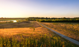 Foto de paisaje de un parque vacacional con glamping, campos, un río y bosque al atardecer.