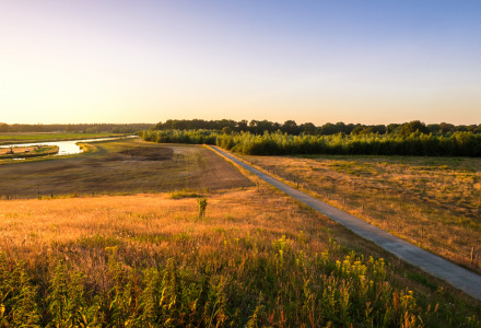 Foto de paisaje de un parque vacacional con glamping, campos, un río y bosque al atardecer.