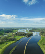 Vista panorámica de un parque vacacional con glamping, campos verdes, ríos serpenteantes y cielo azul.