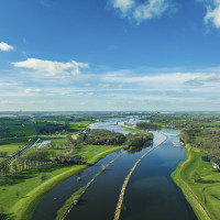 Vista panorámica de un parque vacacional con glamping, campos verdes, ríos serpenteantes y cielo azul.