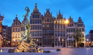 Vista nocturna de la Grote Markt de Amberes con la fuente Brabo y casas gremiales históricas.