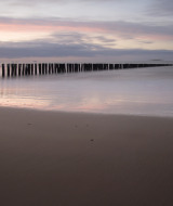 Rustig strand bij zonsondergang nabij Tholen, Zeeland, Nederland, met houten palen in het kalme water.