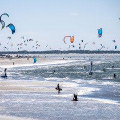 Colorful kites fill the sky as people kitesurf on the beach near a holiday park with glamping options.