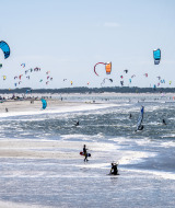 Bunter Strand mit kitenden Menschen und Drachen bei einer Ferienanlage mit Glamping-Unterkünften am Meer.