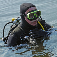 Un buzo con equipo completo y máscara verde está en el agua en un parque vacacional con glamping.