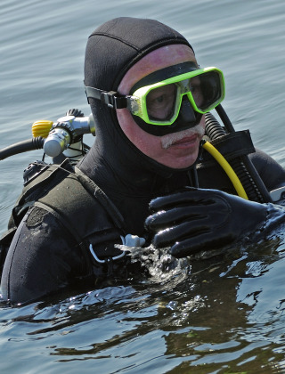 Ein Taucher in kompletter Ausrüstung und grüner Brille ist im Wasser eines Ferienparks mit Glamping.