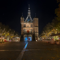 Night view of an illuminated historic building and square with trees adorned with festive lights at a holiday park.