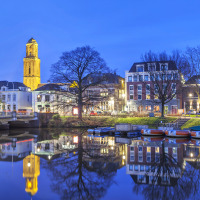 Avondbeeld van een stad aan het water met boten, glamping accommodaties en verlichte toren in vakantiepark.