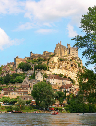 Vista de un pueblo y un castillo en la cima de una colina cerca de Souillac, Occitania, con canoas en el río.
