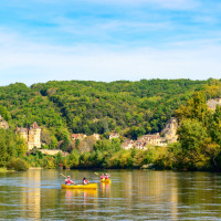 Personas en canoa disfrutan de un parque de vacaciones tipo glamping junto a un río y colinas verdes frondosas.