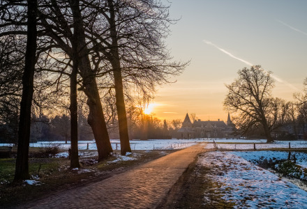 Amanecer sobre paisaje nevado cerca de Enter, Overijssel, Países Bajos, con un sendero hacia un castillo.