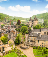 Vista panorámica de un pueblo vacacional con glamping, edificios históricos y un castillo entre colinas verdes.