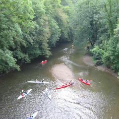 Mensen varen in kano’s op een rivier bij een glamping-vakantiepark, omgeven door groene natuur.