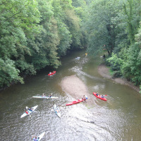 Mensen kanoën op een bosrijke rivier bij een glamping-vakantiepark, omringd door groene bomen.