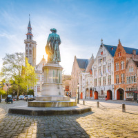 Belgisch plein met gekleurde gevelhuizen, kinderkopjes en centraal een standbeeld bij zonnig weer.