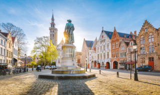Plaza histórica de Bélgica con casas de colores, calles adoquinadas y una estatua central al sol.