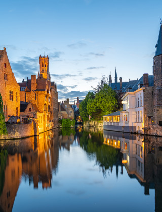 Escena nocturna junto a un canal y edificios históricos en un parque vacacional con glamping en Bélgica.