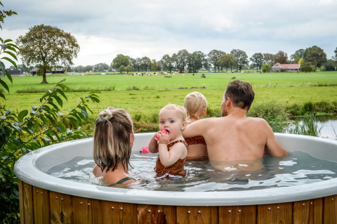 Familie slapper af i et vildmarksbad med udsigt over grønne marker i Holiday Park Mölke, Overijssel.