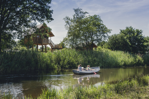 Dos personas reman en un bote por un río junto a una cabaña en los árboles en Holiday Park Mölke, Overijssel.