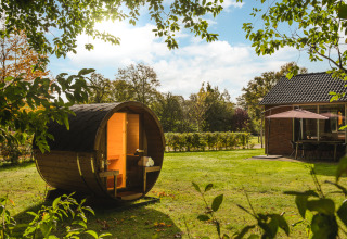 A cozy barrel sauna sits on a green lawn beside a holiday home, with sun shining at Holiday Park Mölke.