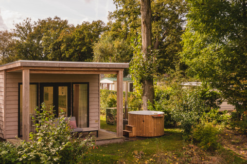 Cabaña de madera con porche y jacuzzi exterior rodeada de vegetación en Holiday Park Mölke, Overijssel.