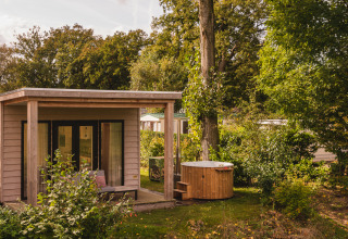 Houten huisje met veranda en buiten bubbelbad tussen het groen op Vakantiepark Mölke in Overijssel.