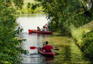Familier padler i røde kajakker på en smal flod omgivet af frodigt grønt i Holiday Park Mölke, Overijssel.