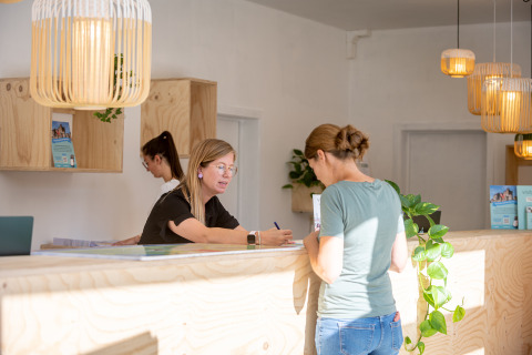 Receptie van Urban-Gardens vakantiepark in Oost-Vlaanderen met gasten en personeel bij de balie.