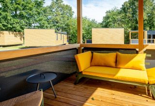 Terras met gele zetel op Urban-Gardens vakantiepark in Oost-Vlaanderen, België, omringd door houten chalets.