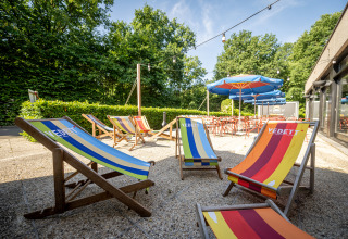 Zonnige buitenruimte bij Urban-Gardens met kleurrijke ligstoelen, parasols en omgeven door groen.