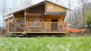 Tienda safari Villatent Ranger en Camping 't Geuldal, Países Bajos, con terraza y hamaca frente césped verde.
