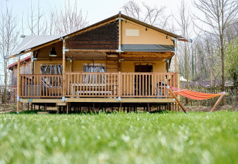 Tienda safari Villatent Ranger en Camping 't Geuldal, Países Bajos, con terraza y hamaca frente césped verde.