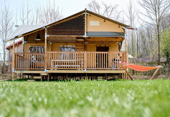 Tienda safari Villatent Ranger en Camping 't Geuldal, Países Bajos, con terraza y hamaca frente césped verde.