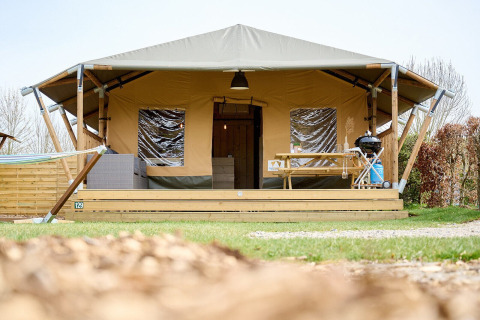 Tienda safari Villatent Cottage en Camping 't Geuldal, Países Bajos, con terraza, mesa y barbacoa fuera.