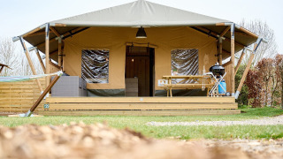 Tienda safari Villatent Cottage en Camping 't Geuldal, Países Bajos, con terraza, mesa y barbacoa fuera.