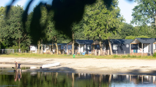 Casas de playa en Camping 't Veld, Países Bajos, junto al lago y árboles, personas en la orilla.