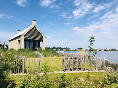 Pequeña casa junto al lago con valla de madera, Villa Oesterdam en Oesterdam Resort en Países Bajos en un día soleado.