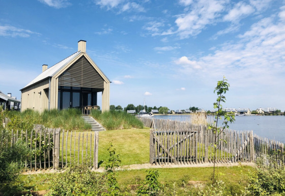 Pequeña casa junto al lago con valla de madera, Villa Oesterdam en Oesterdam Resort en Países Bajos en un día soleado.