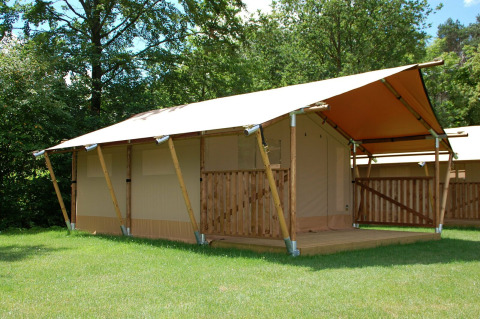 Tienda safari en Baalse Hei, Bélgica, con estructura de madera y porche cubierto rodeado de vegetación.